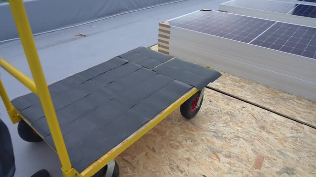 A worker pushes a cargo cart to load and transport solar panels. Preparing materials before installation.