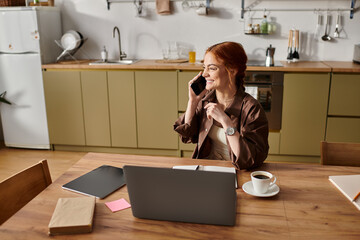 Charming red haired woman enjoying a warm coffee while on a phone call in her cozy kitchen