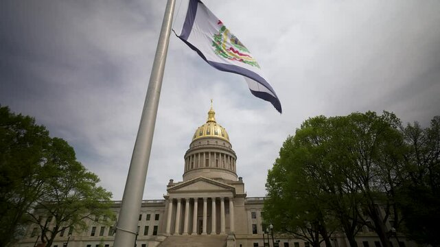 Visitors admire the impressive stone architecture of West Virginias state capitol in Charleston, framed by vibrant trees and the state flag waving proudly.
