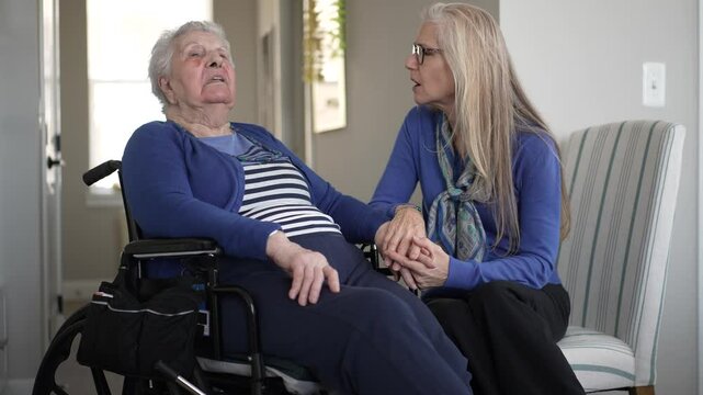 An elderly woman in her 90s receives affectionate support from her daughter while seated indoors. Their cozy interaction reflects love and togetherness in daily life.