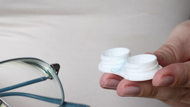 closeup of female hands holding eyeglasses in one hand and open contact lens case with soft lens in the other, decision between vision correction methods. concept of optometry