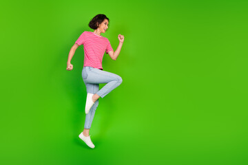 Young woman in a striped t-shirt and jeans jumping joyfully against a vibrant green background, expressing energy and liveliness