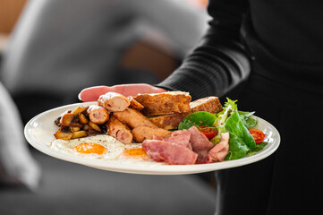A plate with a traditional English breakfast, including sausages, fried eggs, mushrooms, bacon,...