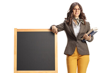 Young female teacher leaning on a blank blackboard