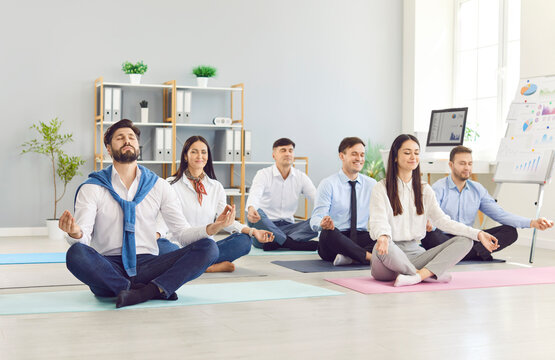 Team of corporate office employees having yoga and meditation workout for body and mind. Group of happy calm relaxed people meditating and recharging with energy for both physical and mental wellness