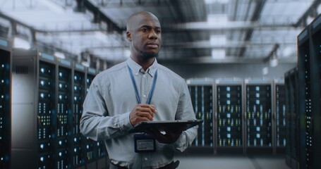 Big Data Center with Server Racks: Professional African American Specialist Using Tablet Computer,...