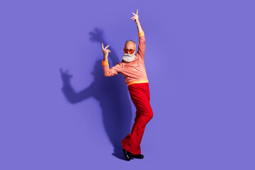 Elderly fashionable man with grey beard in stylish retro costume dancing against a vibrant purple background, fun and trendy