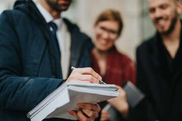 Group of business professionals conferring together while reviewing notes and ideas outdoors in a casual environment.