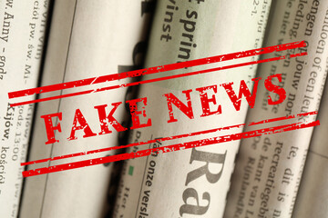 Red Fake News stamp and newspapers in different languages as background, closeup