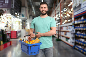 Man holding shopping basket with different food products at supermarket