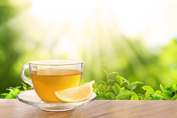 Cup of green tea and lemon wedge on wooden table in tea plantation. Space for text