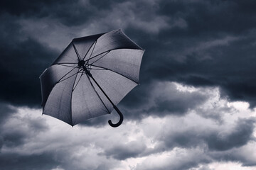 Black umbrella flying in dark cloudy sky. Stormy weather