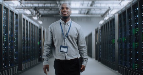 Fototapeta premium Big Data Center with Server Racks: Professional African American Specialist with Tablet Computer Walking In Warehouse. Internet Servers, Information Technology, Cyber Security and Telecommunications.