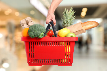 Man holding shopping basket with different food products at supermarket, closeup