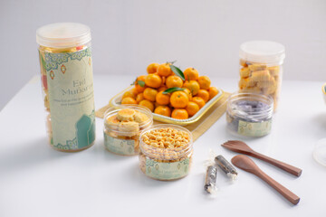 Eid hampers containing dry cakes in jars such as nastar, roasted peanuts without skin, oranges, and sweets on a white background with typical Eid ornaments