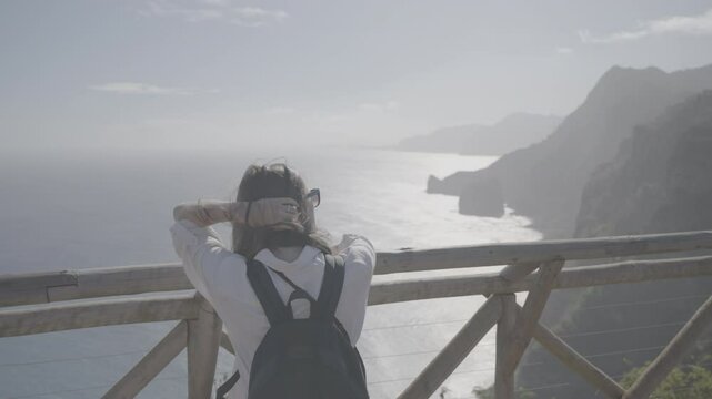 Back view of woman facing Atlantic coast cliffs under bright sun from high point on Madeira island (SLOG3)