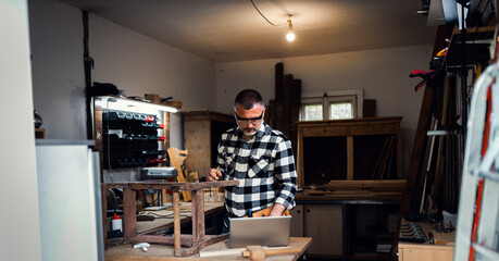 Carpenter standing in his workshop restoring old piece of furniture marking measurements on wood...