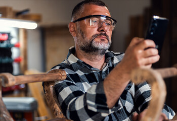 Portait of carpenter looking at his mobile phone in his workshop.