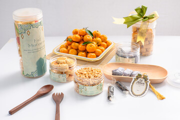 Eid hampers containing dry cakes in jars such as nastar, roasted peanuts without skin, oranges, and sweets on a white background with typical Eid ornaments