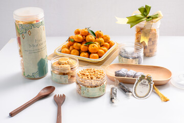 Eid hampers containing dry cakes in jars such as nastar, roasted peanuts without skin, oranges, and sweets on a white background with typical Eid ornaments