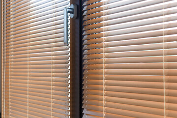 A detailed view of wood blinds up close. Venetian blinds with 25 mm slats are installed on aluminum window sashes. Cable fixation of the blinds. A sleek metal handle contrasts the warm tones.
