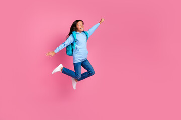 Excited young girl joyfully jumping with arms raised against a pink background, showcasing happiness and youthful energy