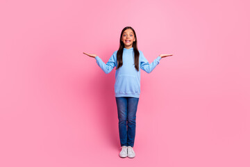 Charming young girl wearing a blue hoodie poses against a pink background, with cheerful gestures and joyful expression