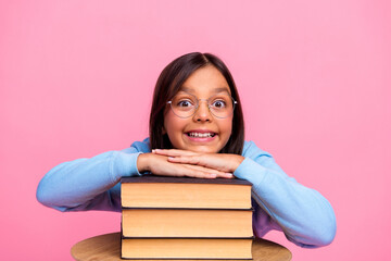 Smiling girl in trendy sweatshirt and glasses posing with stack of book against a cheerful pink...