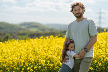 Father and daughter hugging in front of blooming yellow rapeseed field. Family emotions and leisure...