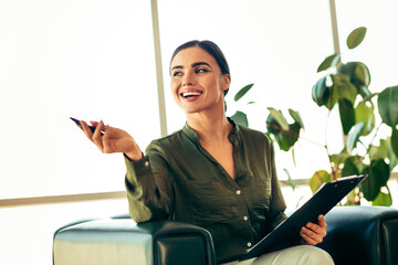 Confident businesswoman holding a document with a bright smile while sitting in a modern office...