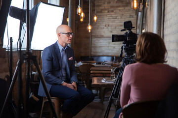 Professional videographer filming an interview with a businessman in a restaurant, using professional lighting and sound equipment