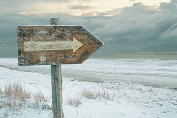 Naklejka premium Weathered wooden arrow sign on snowy beach points left