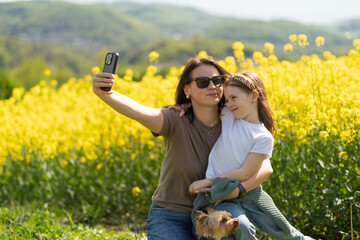 Daughter and mother hugging and smiling taking selfie in front of blooming yellow rapeseed field....