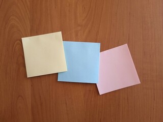 Three colored square note papers on wooden background