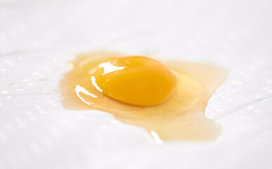 Bright yellow egg yolk rests on textured white surface. Soft lighting highlights yolks glossy texture, contrasting with absorbent background. Close-up captures culinary simplicity