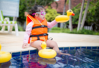 A little girl wearing a life jacket is getting ready to go into a swimming pool,happy toddler baby...
