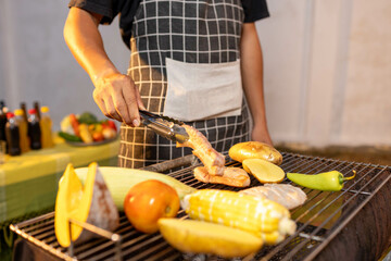 A man enjoys a summer barbecue outdoors, grilling meat and vegetables over open flames, surrounded by friends, smoke, drinks, and weekend freedom.
