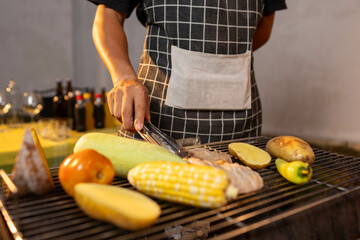 A man enjoys a summer barbecue outdoors, grilling meat and vegetables over open flames, surrounded by friends, smoke, drinks, and weekend freedom.
