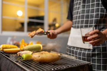 A man enjoys a summer barbecue outdoors, grilling meat and vegetables over open flames, surrounded by friends, smoke, drinks, and weekend freedom.
