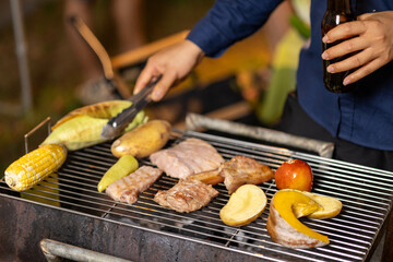 A glowing barbecue grill sizzles with assorted meats and vegetables, flames and smoke rising in the dark, capturing the essence of a summer cookout.
