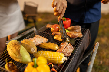 A vibrant summer gathering comes to life as men and women celebrate around a sizzling barbecue. With flames dancing on the grill and fresh vegetables alongside savory meats, the group shares drinks, l