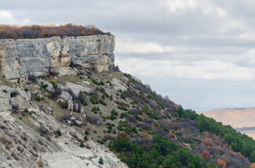 Steep cliff face overlooks lush mixed vegetation under overcast skies. Rugged rocks dominate...