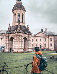Man is admiring the monument  in travel 
Is wearing backpack hat  and raincoat the weather is cloudy and droping light rain