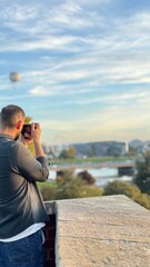 Man is photoshooting the landcape before the sunset in travel 
Is wearing shirt and the weather is perfect and the large ballon is in the sky