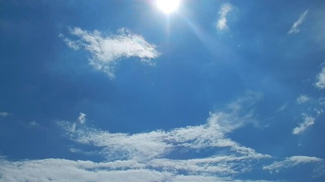 Blue sky, sun rays, moving decorative white clouds and Cloud iridescence, Irisation - natural sky background. Topics: sunny, summer, calm, optimistic sky, optical phenomenon, weather, air space