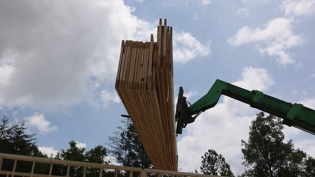 Forklift telehandler crane lifts large wooden truss into place, helping to construct new home under works day