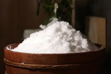 Coarse white salt piled in a traditional wooden basket, softly lit with a natural and rustic background, representing traditional food preservation and seasoning.    