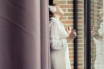 Enjoying beautiful сaucasian young woman in headphones listening music dancing near big panoramic window.