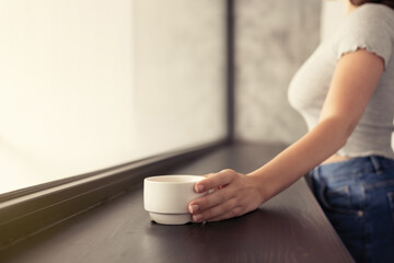 Beautiful сaucasian young woman drinking hot coffee from cup and looking at window.