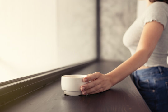 Beautiful сaucasian young woman drinking hot coffee from cup and looking at window.